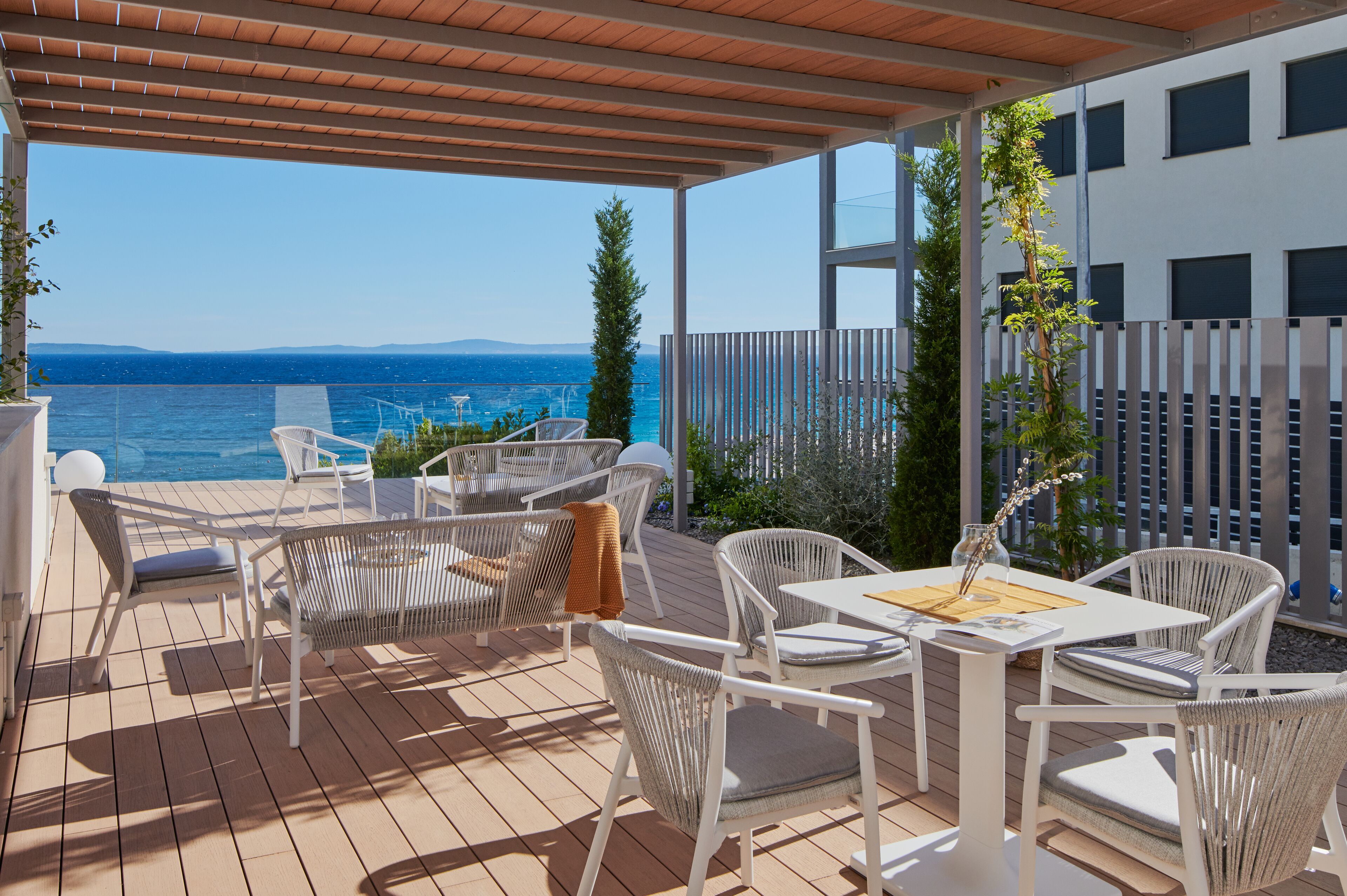 A covered outdoor area with wicker furniture, a table, and a view of the sea.