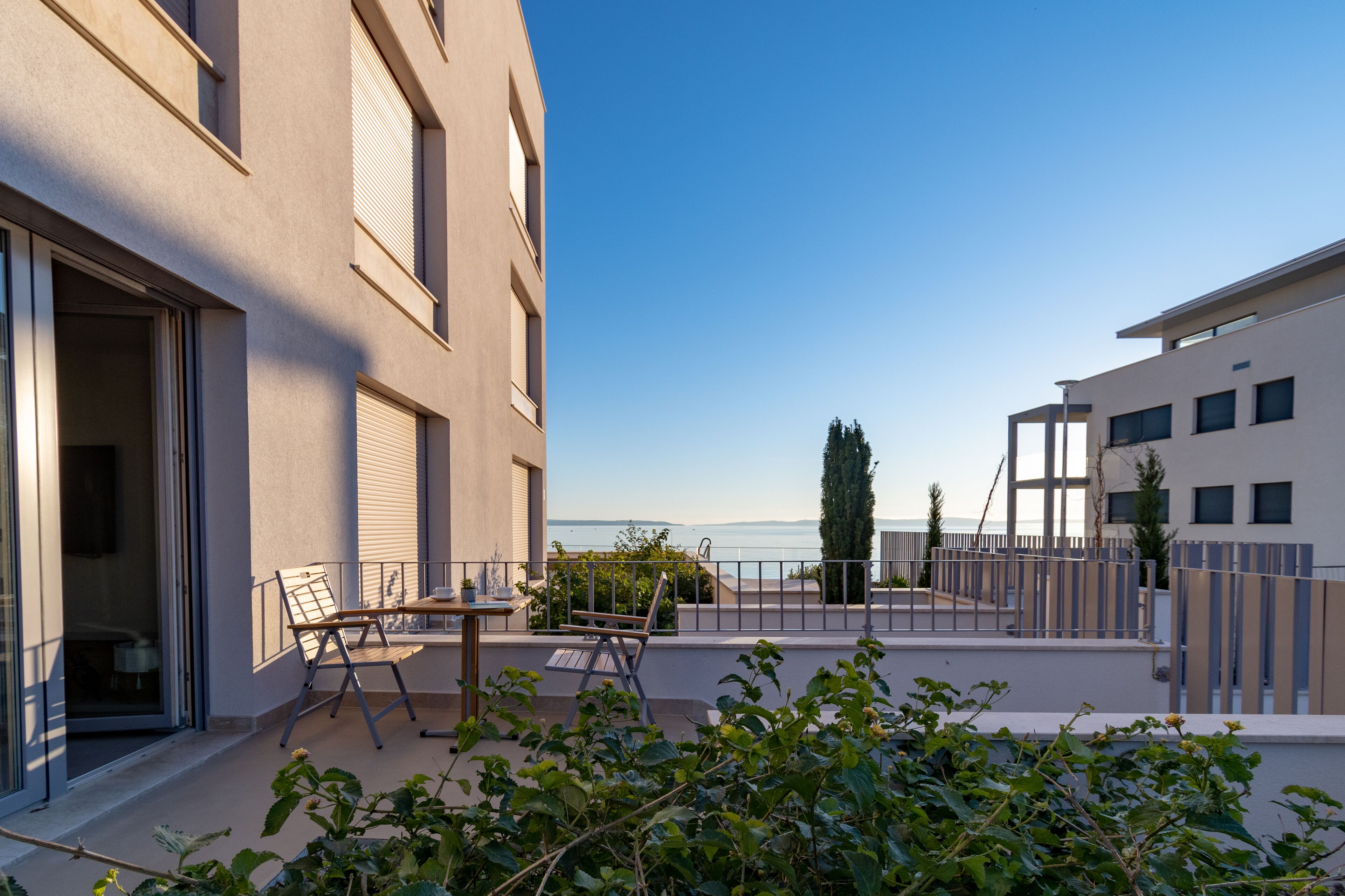 A modern building with a balcony, outdoor seating, and a view of the sea.