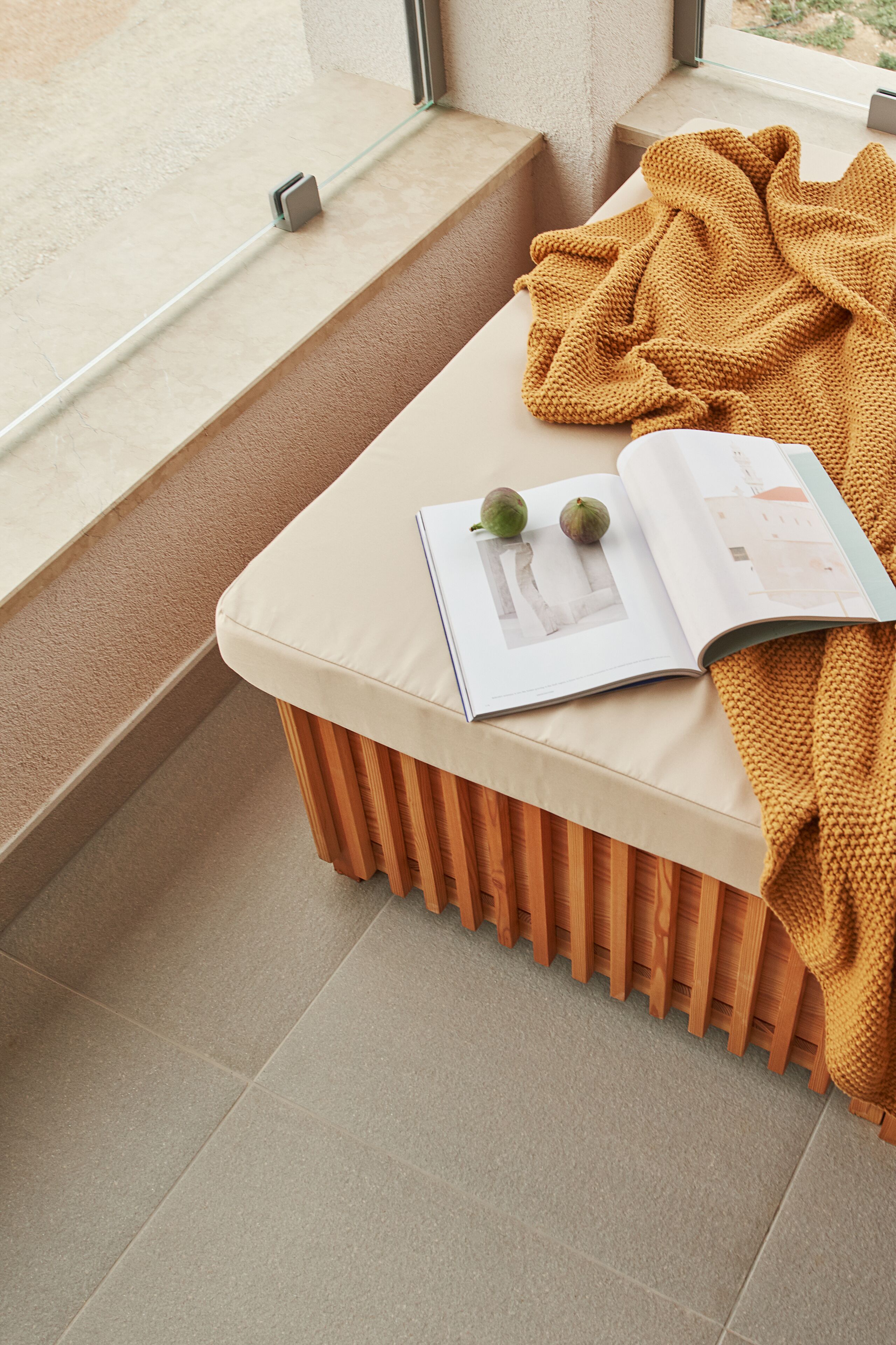 A reading nook with a cushioned bench, a book, and a blanket.