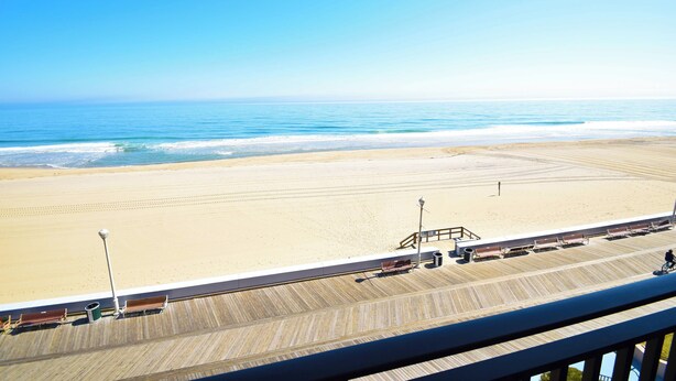 A beach view from a balcony with a wooden deck, a lifeguard tower, and a clear blue sky. - Ocean Hideaway 404-Oceanfront 18th St, Free WiFi, Elev, W/D, AC (Ocean City)
