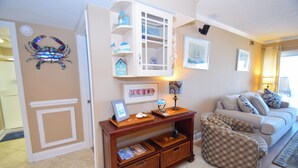 A living room with a wooden console table, a white cabinet, a couch, and a decorative crab wall art. - Ocean Hideaway 404-Oceanfront 18th St, Free WiFi, Elev, W/D, AC (Ocean City)