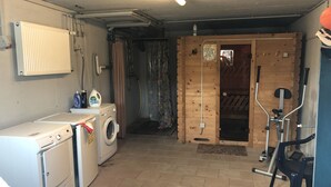 A laundry room with a washing machine, dryer, and ironing board. There is a wooden door leading to another room. - FeWo Schloß Ramspau - Forsthaus Ostwohnung (5-star DTV) (Ramspau)