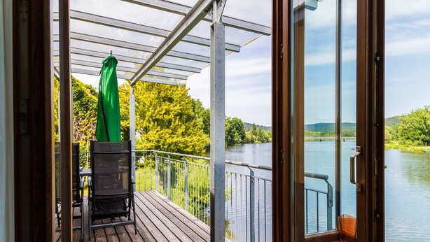 A wooden deck with a grill, a green umbrella, and a view of a lake and trees. - FeWo Schloß Ramspau - Forsthaus Ostwohnung (5-star DTV) (Ramspau)