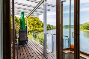 A wooden deck with a grill, a green umbrella, and a view of a lake and trees.