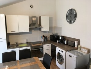 A compact kitchen with white cabinets, a stainless steel range hood, a microwave, a coffee maker, and a washing machine.