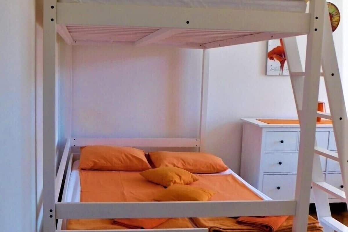 A bunk bed with a white frame and orange bedding.