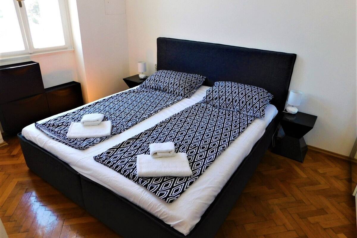 A double bed with a black headboard, two bedside tables with lamps, and a window with a view of trees.