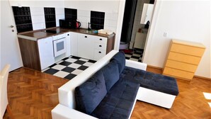 Un espacio habitable compacto con kitchenette, sofá y suelo de madera.