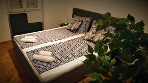 Una cama bien hecha con ropa de cama estampada, una mesita de noche con lámpara y una planta en maceta.