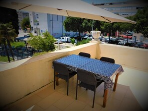 Una terraza con mesa y sillas, una sombrilla y vistas a un estacionamiento y edificios.