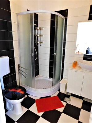 Un baño moderno con ducha de vidrio, inodoro blanco y lavamanos con espejo.
