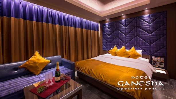 Una habitación de hotel con cama, sofá, mesa con botella y vasos, y un cabecero decorativo.