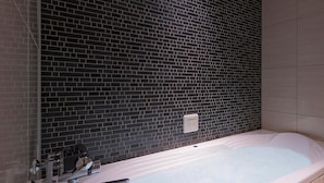 Un baño con pared de azulejos negros, una bañera y una zona de ducha.