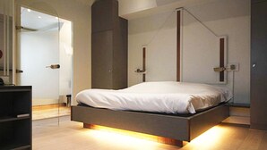 A modern bedroom with a bed, built-in shelving, and a unique lighting feature under the bed. - Hostellerie Klokhof (Kortrijk)