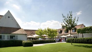 A courtyard with a white building, a tree, and umbrellas. - Hostellerie Klokhof (Kortrijk)