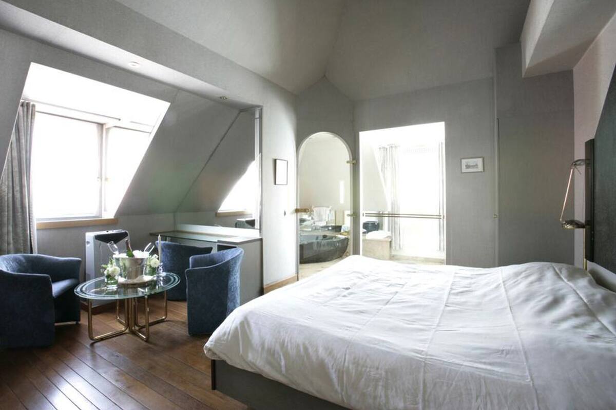 Un dormitorio moderno con una cama grande, una mesa de vidrio con sillas y vistas a la ciudad a través de tragaluces.