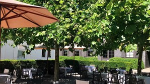 An outdoor dining area with tables and chairs, surrounded by trees and a building in the background. - Hostellerie Klokhof (Kortrijk)