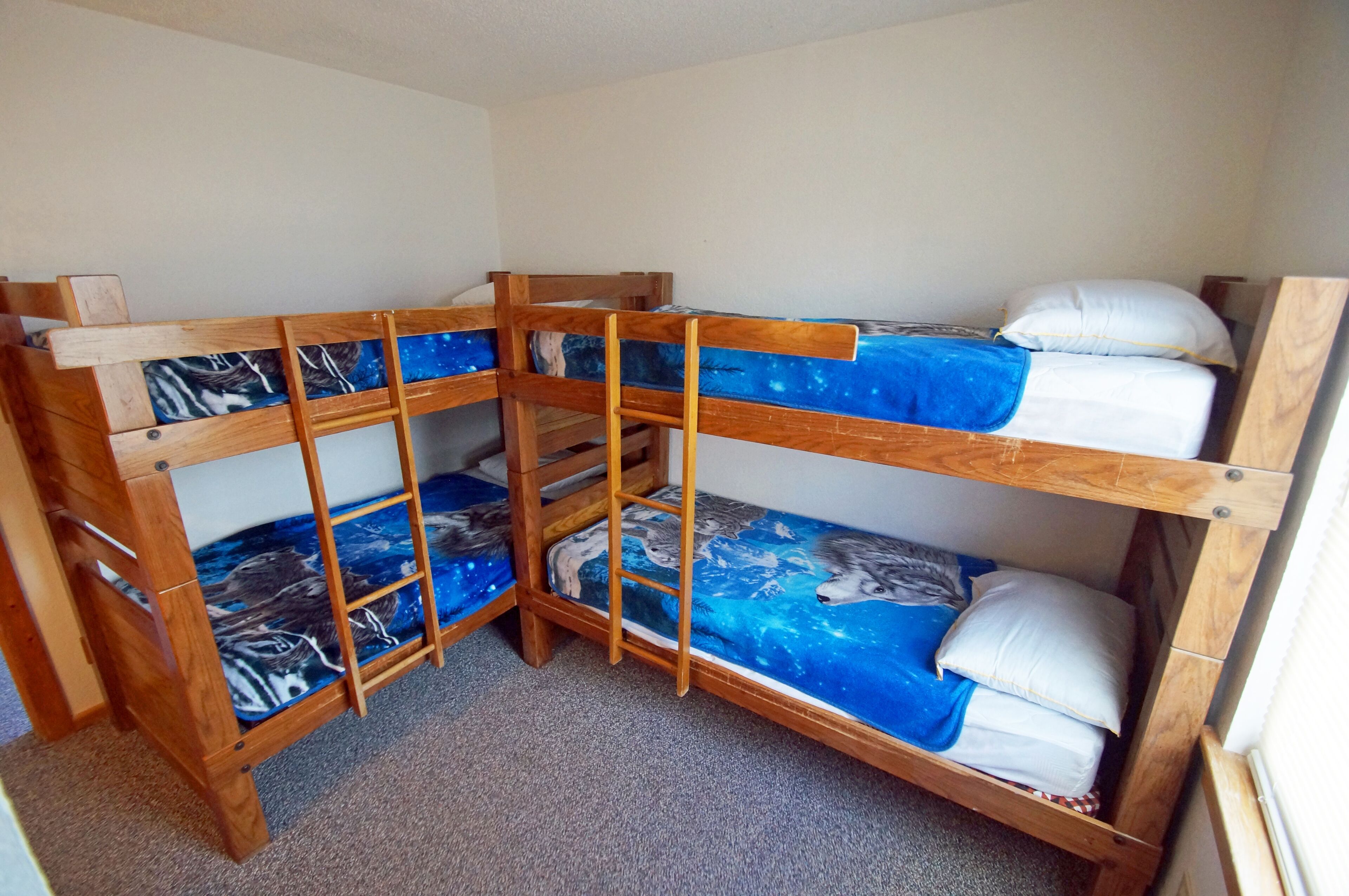 Ein Zimmer mit drei Etagenbetten aus Holz, jeweils mit einem blauen, raumfahrt-inspirierten Schutzbezug.