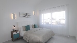 Een moderne slaapkamer met een groot bed, een nachtkastje en een raam met dunne gordijnen.