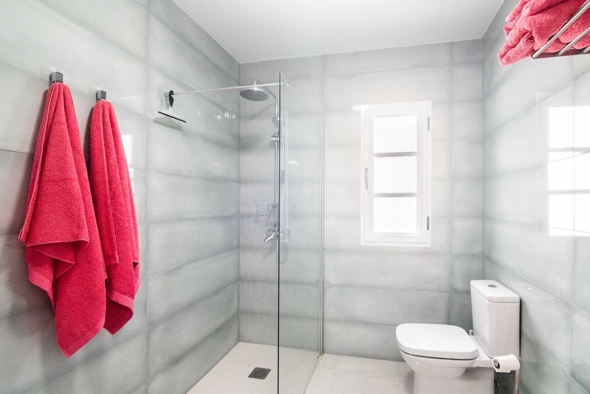 Une salle de bain moderne avec une douche à parois de verre, des toilettes et une fenêtre.