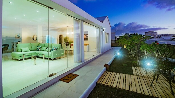 Een modern huis met een glazen gevel, een groene bank en een houten terras.