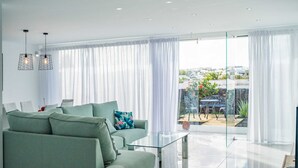 Een moderne woonkamer met een groene bank, een glazen salontafel en uitzicht op een balkon met tuinmeubels.