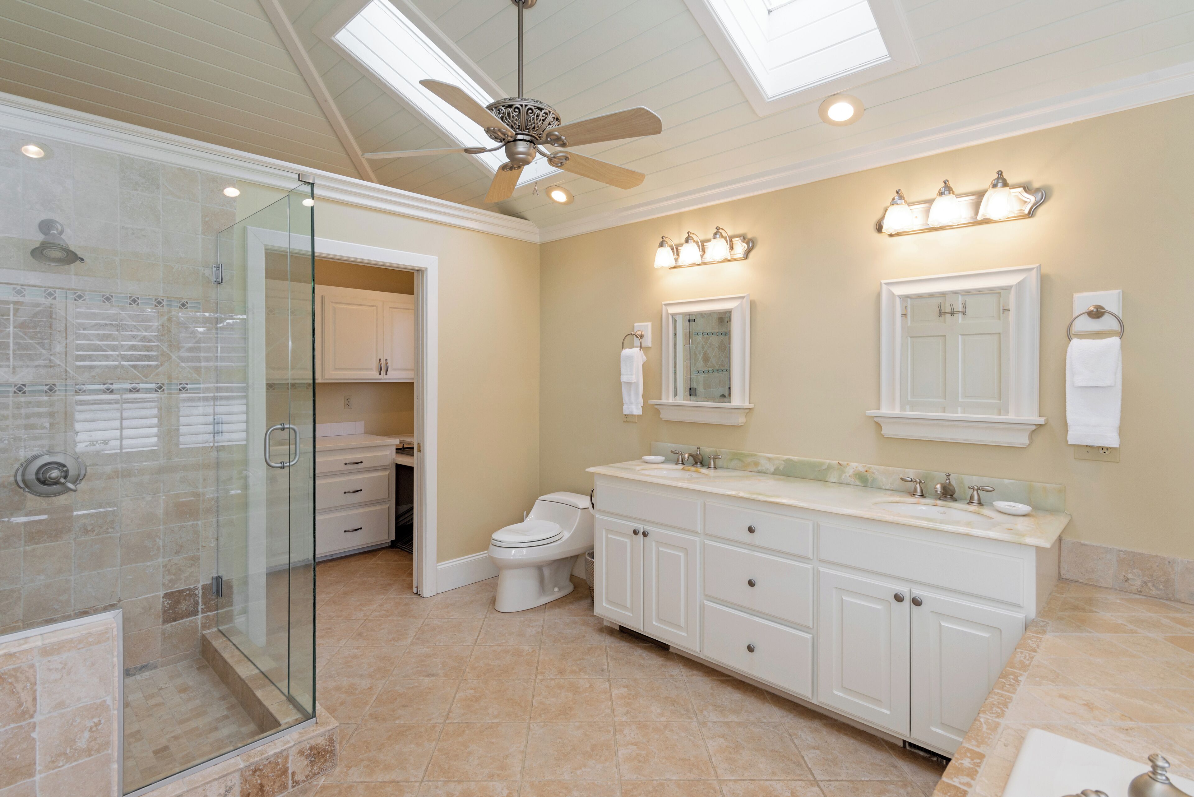 A spacious bathroom with a glass-enclosed shower, a vanity with a sink and mirror, and a ceiling fan.