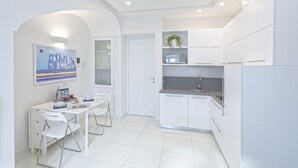 A modern kitchen with white cabinetry, a dining area with white chairs, and a painting on the wall. - Turchese choose to live an emotion (Ischia)