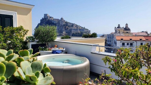 A rooftop terrace with a hot tub, potted plants, and a view of a historic castle on a hill. - Turchese choose to live an emotion (Ischia)