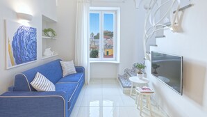 A modern living room with a blue sofa, a flat-screen TV, and a large window with a view of buildings. - Turchese choose to live an emotion (Ischia)