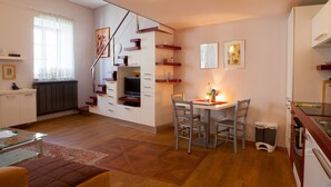 Ett kompakt bostadsutrymme med matplats, litet kök och en trappa.