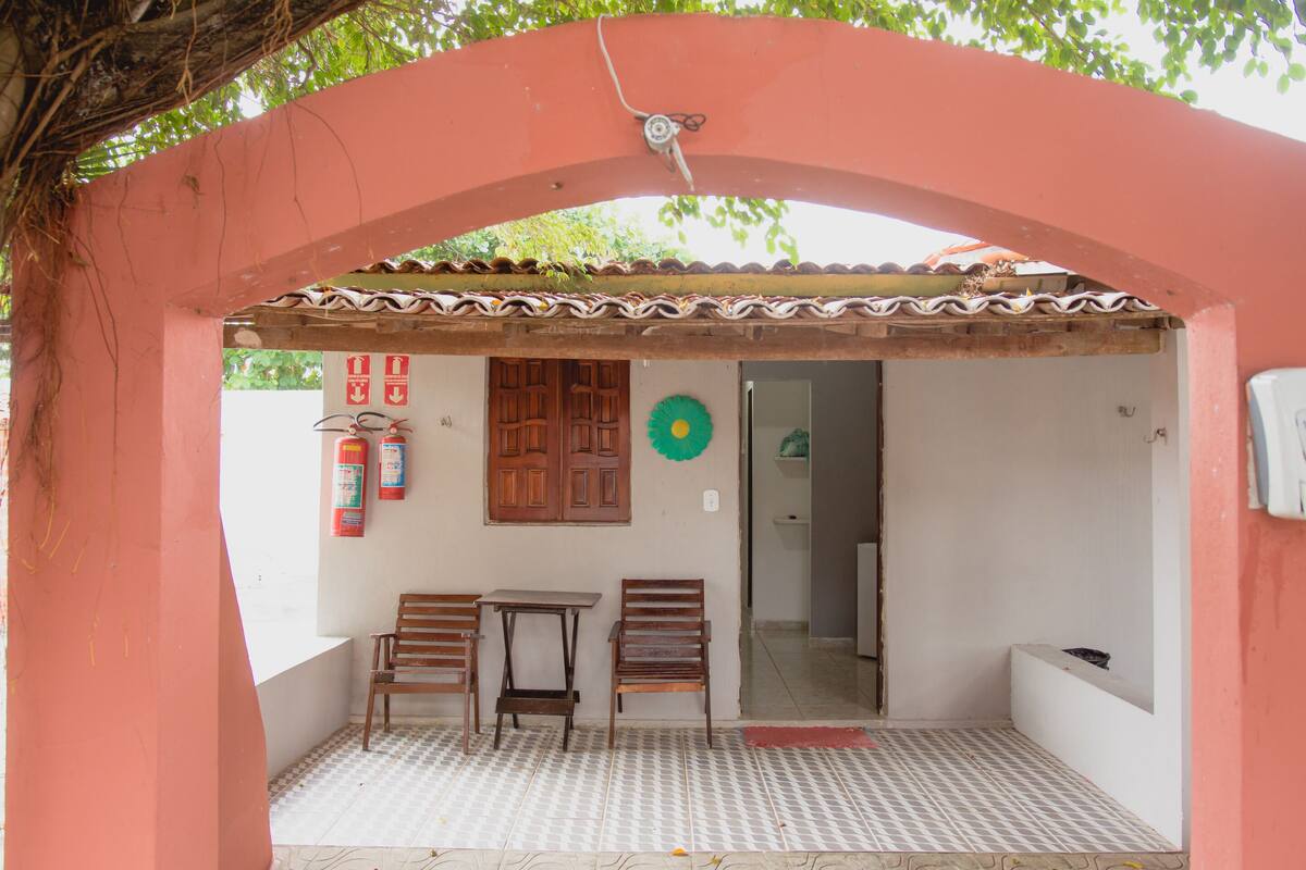 A covered outdoor seating area with two wooden tables and chairs, a tiled floor, and a door leading inside.