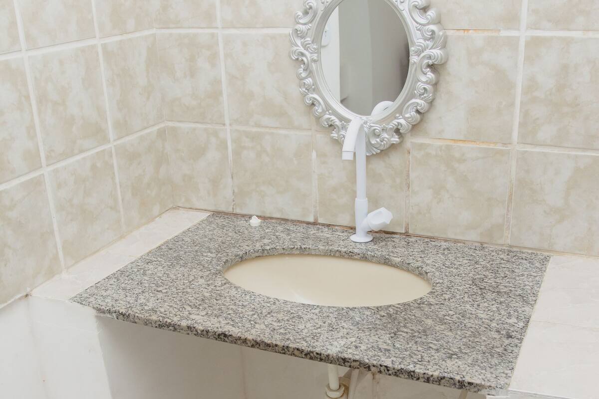 A bathroom with a granite countertop sink, a white mirror with an ornate frame, and tiled walls.