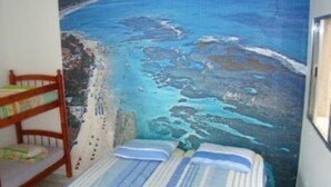 A bedroom with a bed, a wooden chair, and a painting of a beach scene. - Pousada Aconchego (Peruíbe)
