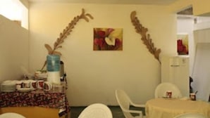 A room with a dining table, chairs, a water dispenser, and a small table with cups and plates. - Pousada Aconchego (Peruíbe)