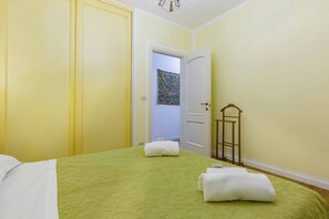 A hotel room with a bed, two towels, a door, and a wall with a tapestry.