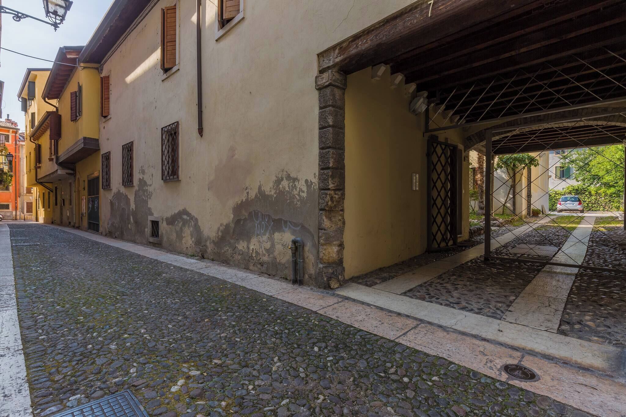 Une ruelle étroite pavée, bordée de bâtiments des deux côtés, avec une entrée couverte et une voiture garée au fond.