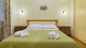 A hotel room with a bed, two bedside tables, a nightstand, a wall-mounted light fixture, and a decorative plate above the bed.
