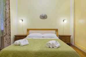 A hotel room with a bed, two bedside tables, a nightstand, a wall-mounted light fixture, and a decorative plate above the bed.