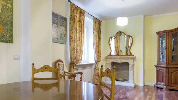 A dining area with a wooden table and chairs, a fireplace with a mirror above it, and a cabinet to the right.