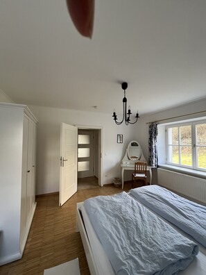 Un dormitorio con una cama, un tocador, un escritorio con una silla, un espejo y una ventana con cortinas.