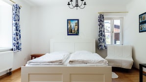 A bedroom with a large bed, a small bedside table, a white sofa, and a window with curtains.