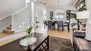 A spacious living area with a dark wooden coffee table, a vase of white flowers, and a modern chandelier. - ⛱ Solterra Resort - 5★Clubhouse - Extended Pool & Spa - Stunning Lakeview Home ☀ (Davenport)