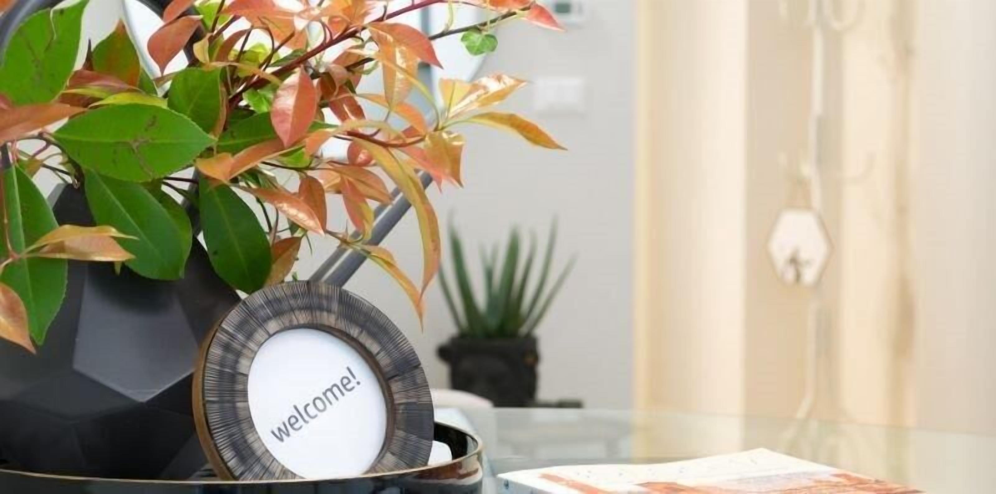 A reception area with a welcome sign, a potted plant, and a glass table.