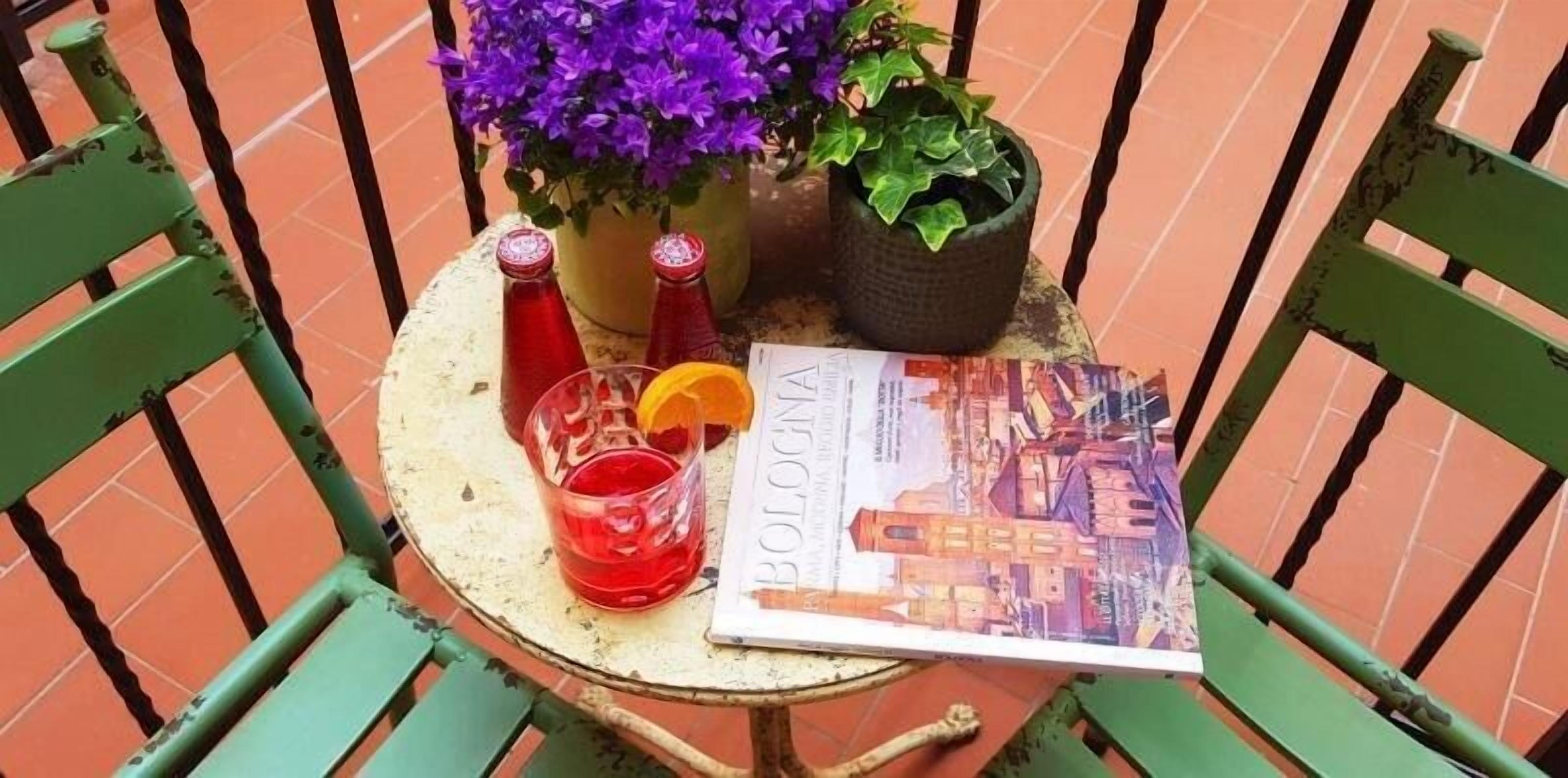A table with a red drink, a book, and two bottles on a tiled patio.