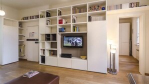Una sala de estar con una estantería, un televisor y un otoman marrón.