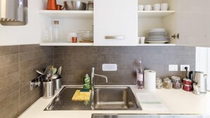 Una cocina moderna con un lavamanos de acero inoxidable, una tetera y diversos utensilios de cocina.