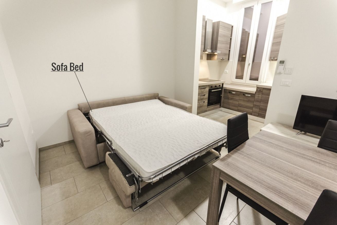 A compact room with a sofa bed, a small kitchen area, and a dining table.