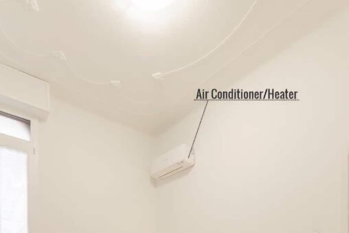 A bedroom with a bed, bedside tables, an air conditioner/heater, and a window.