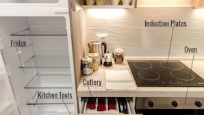 A compact kitchen with labeled sections including a freezer, fridge, induction plates, oven, cutlery, cups, and pans. - S.Felice apartments (Bologna)